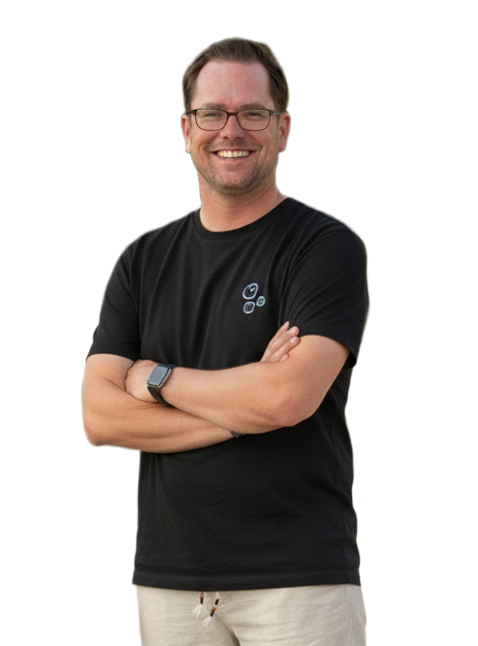 Ein lächelnder Mann mit Brille und schwarzem T-Shirt, die Arme verschränkt.